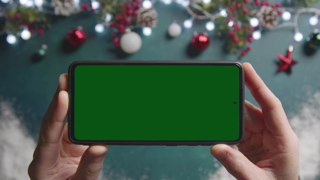 Руки держат смартфон с зелёным экраном на рождественском фоне