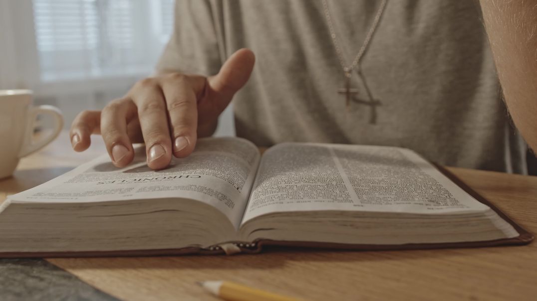 Человек читает книгу библию, водя по ней пальцем