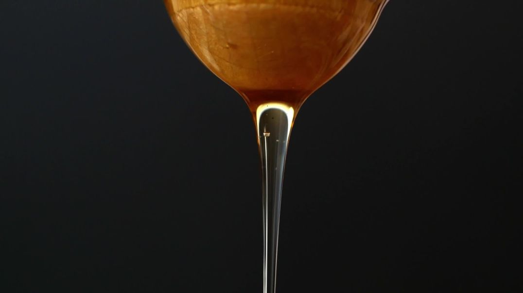 Мёд стекает с деревянной ложки на чёрном фоне